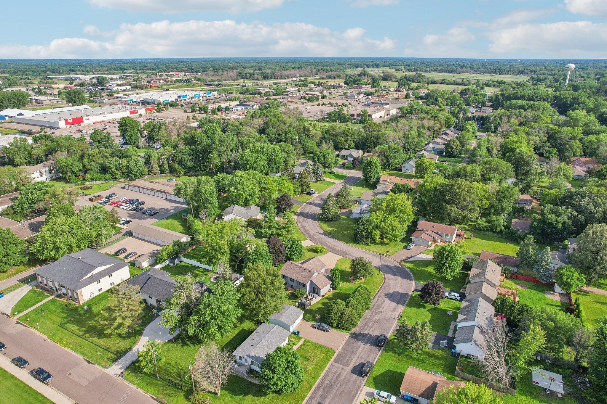 Aerial view of a leafy neighborhood with curving streets and shopping areas in the distance.