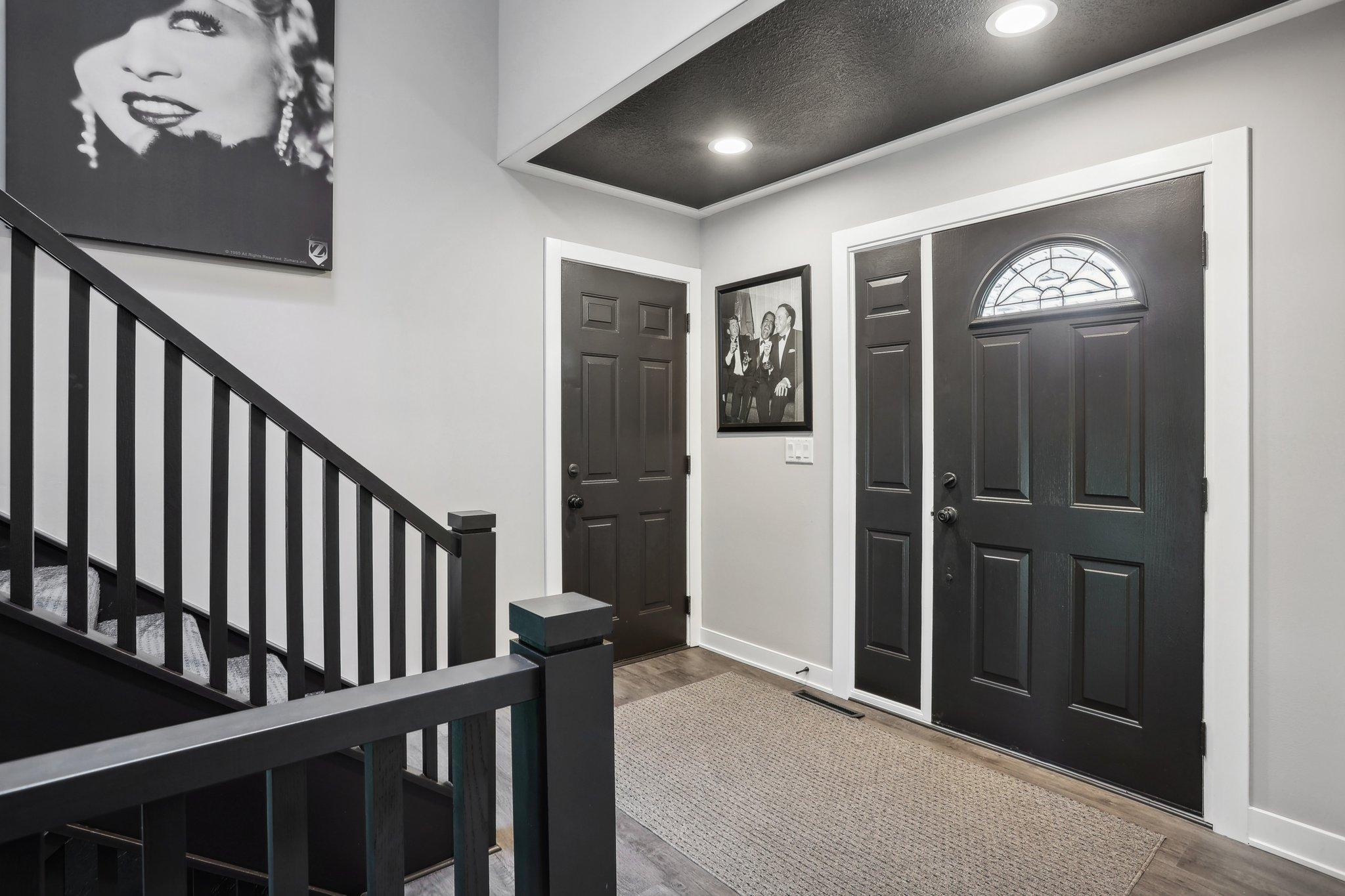 Entryway with a black front door, semicircular window, and staircase with dark railings.