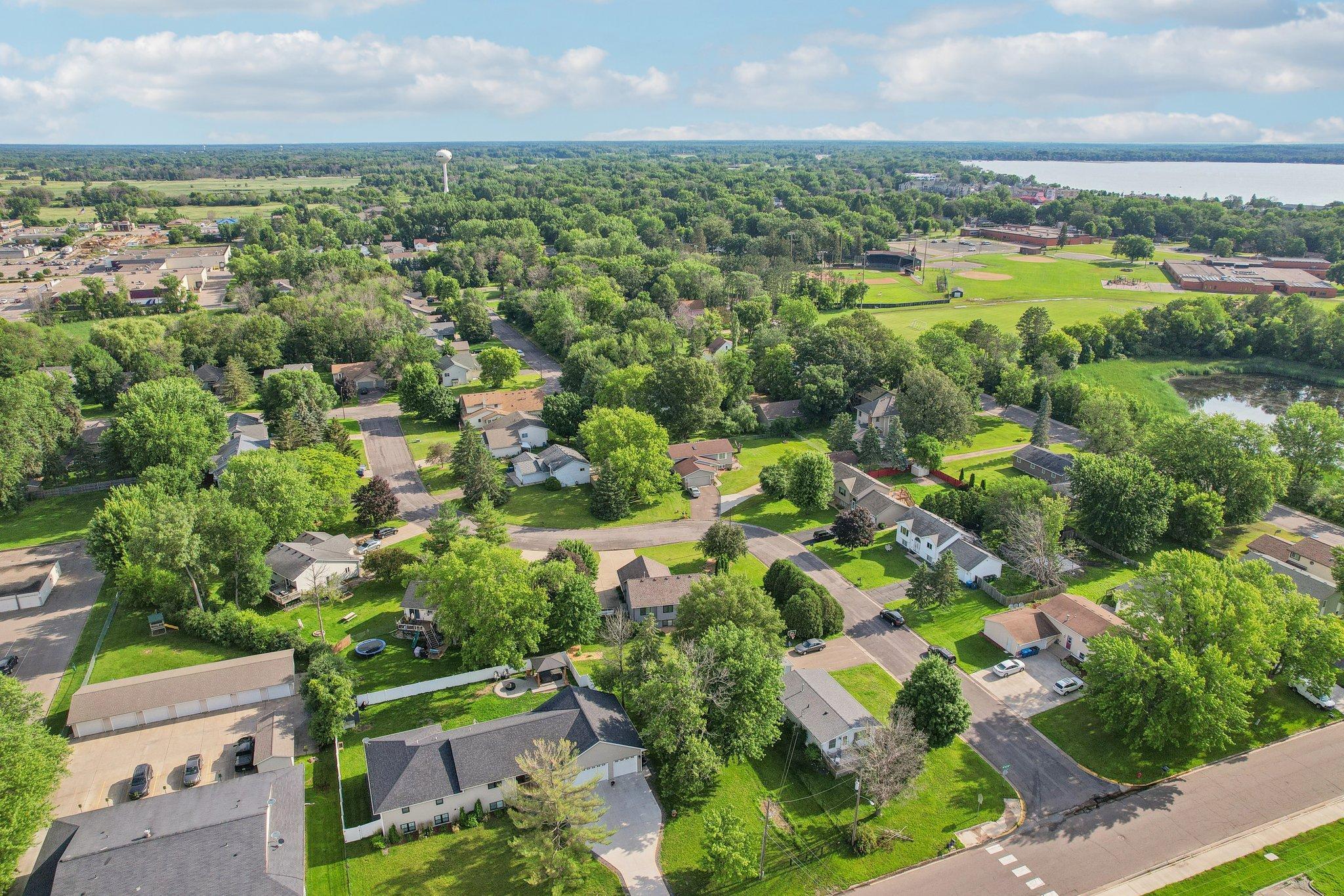Aerial view of a leafy neighborhood, with sports fields and a lake in the distance.