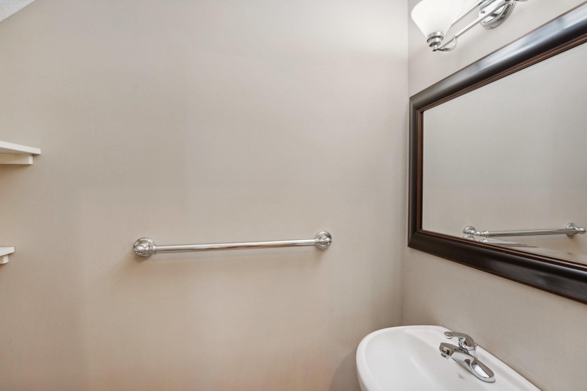 Bathroom with a chrome grab bar, white sink, dark-framed mirror, and small wall shelves.