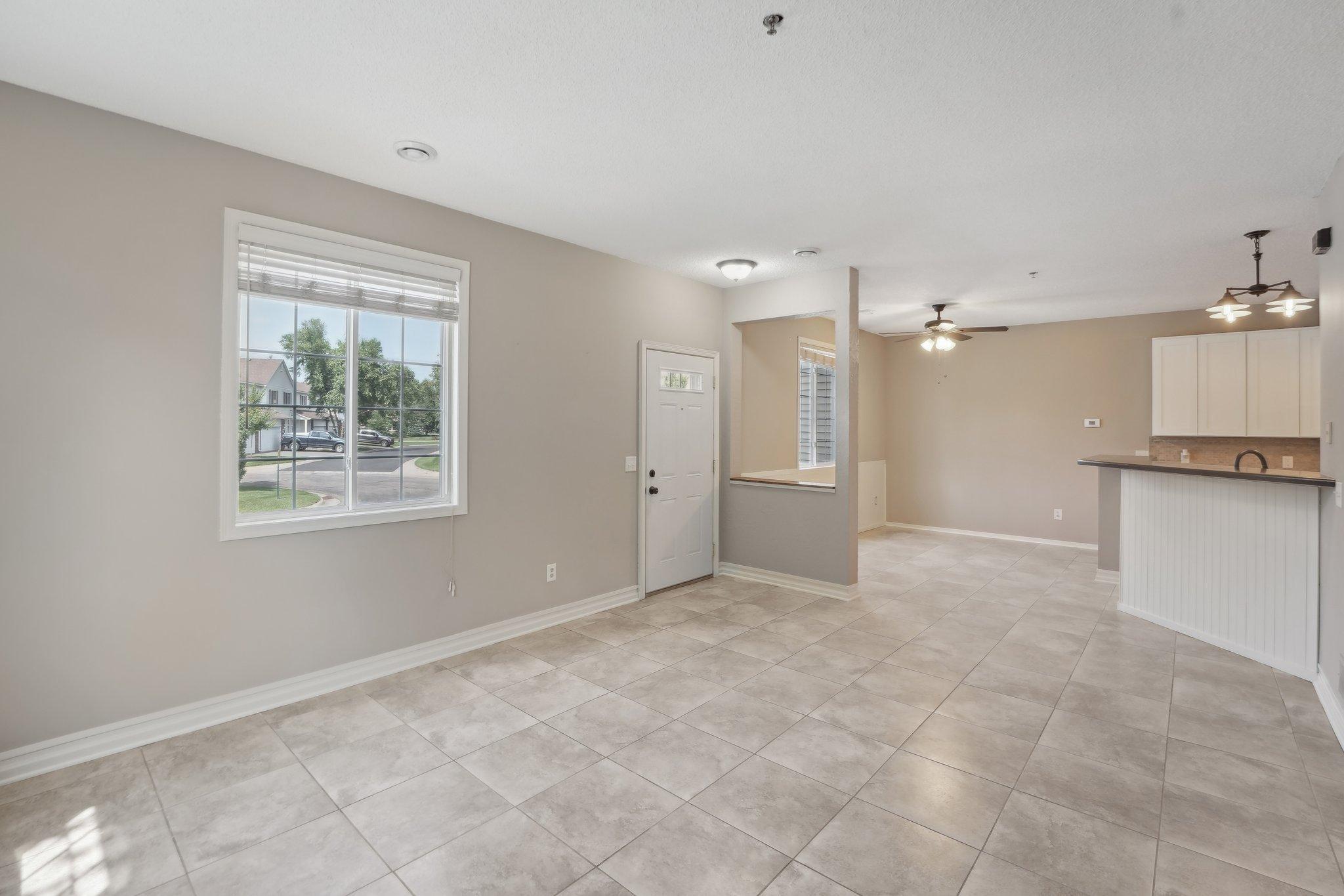 Open-plan interior with tiled floors, a large window, front entry, and kitchen peninsula.