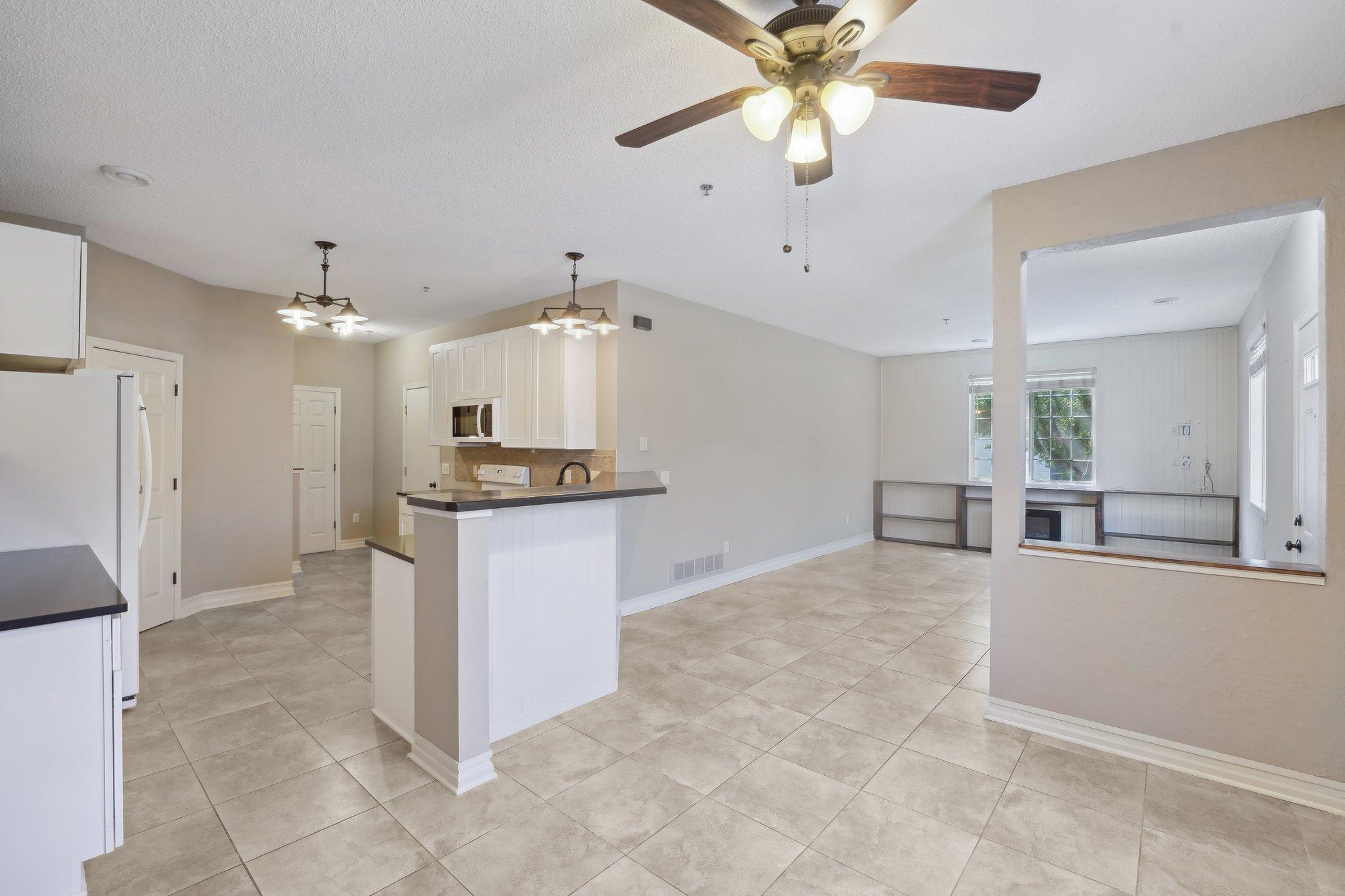 Open-plan kitchen with white cabinets, a breakfast bar, tiled floors, and adjoining windowed room with built-in seating.