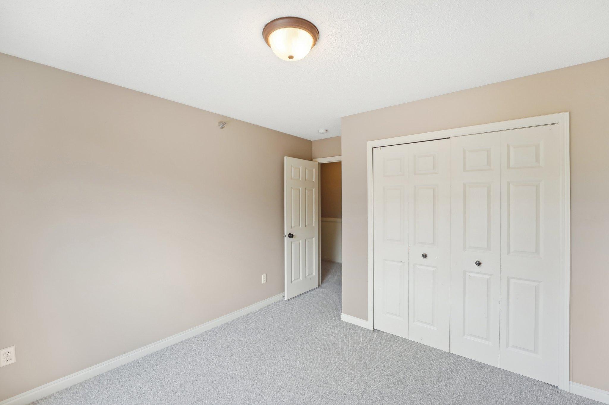 Empty bedroom with gray carpeting, white closet doors, and an open doorway.