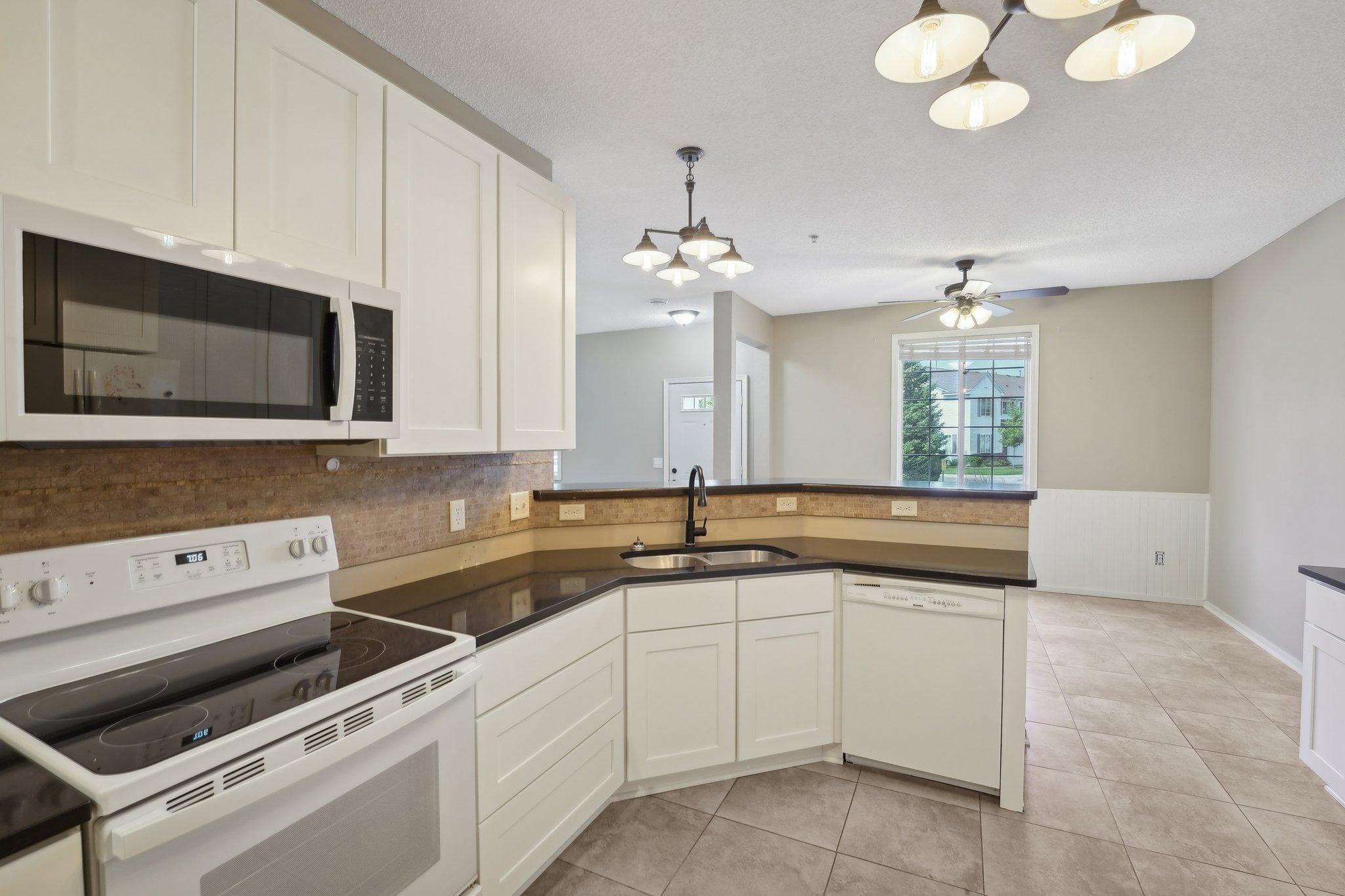 Kitchen with white cabinets, dark counters, tiled backsplash, and an adjoining dining area.