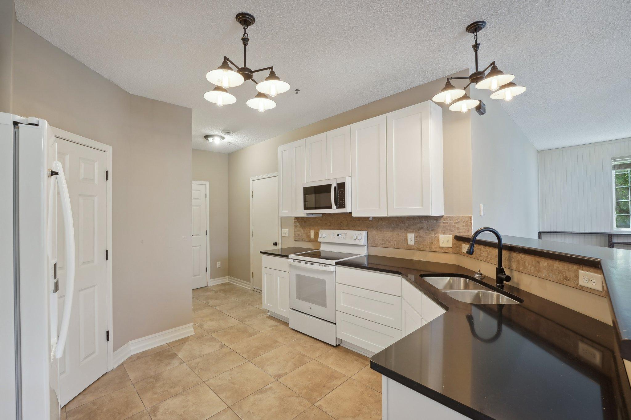 Kitchen with white cabinetry, dark countertops, a double-basin sink, and tan tile flooring.