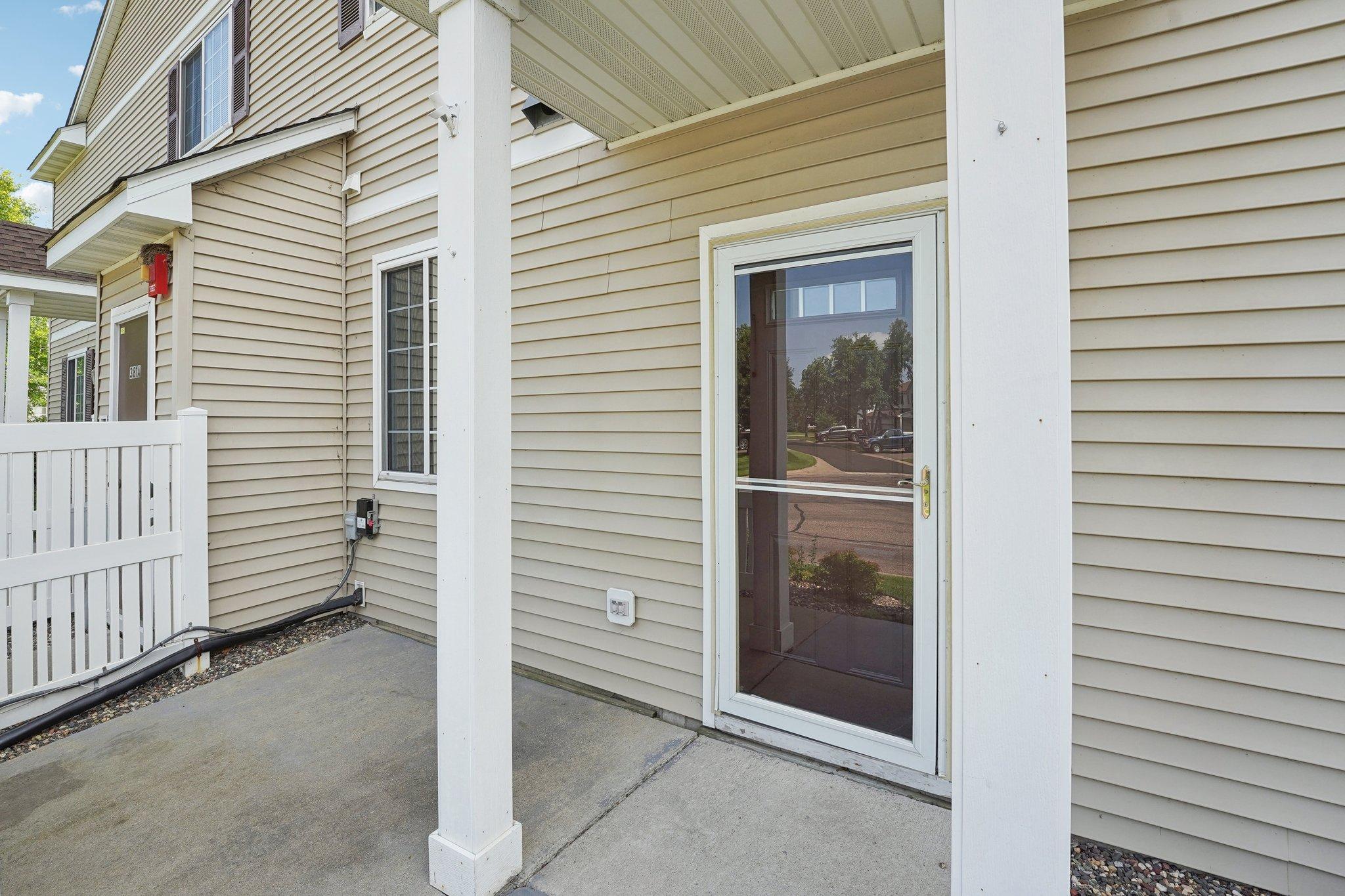 Covered concrete patio with white posts, railing, and a glass storm door.