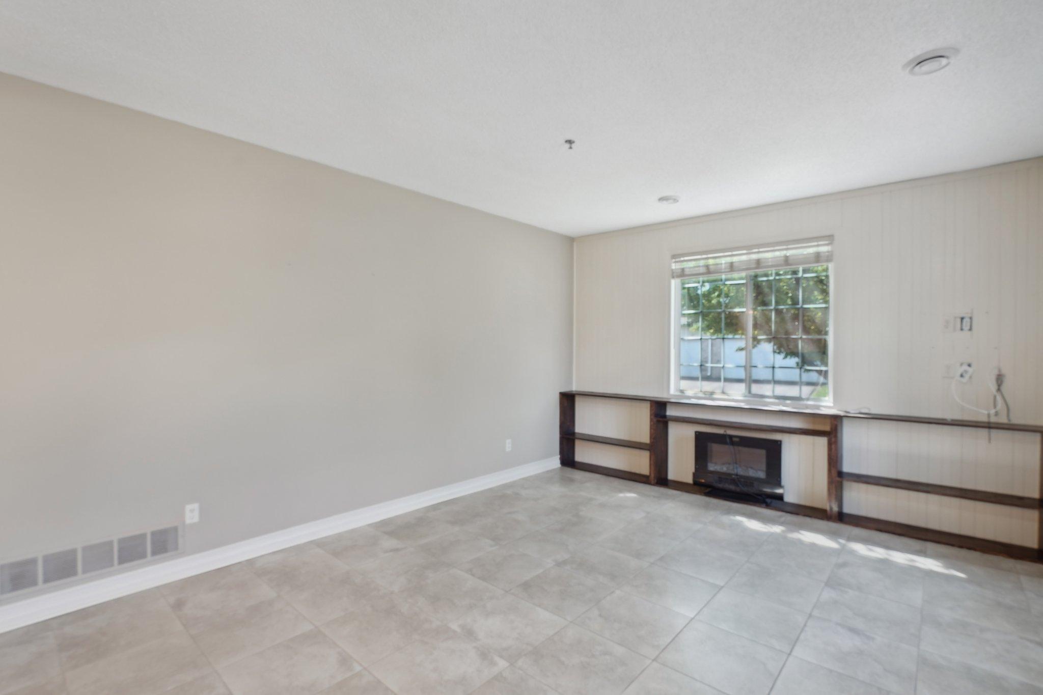 Empty living room with tiled floor, a large window, and built-in entertainment unit surrounding a fireplace.