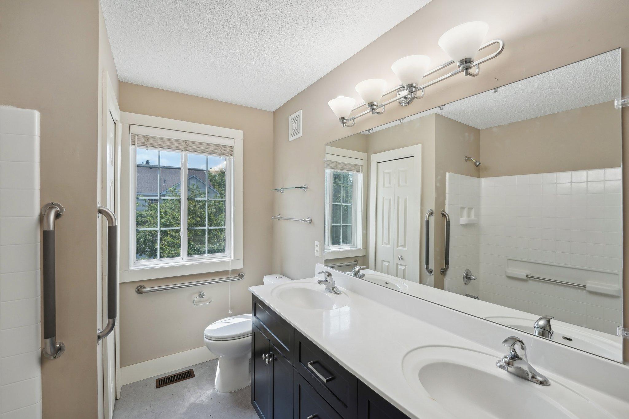 Bathroom with a double-sink vanity, large mirror, and accessibility grab bars.