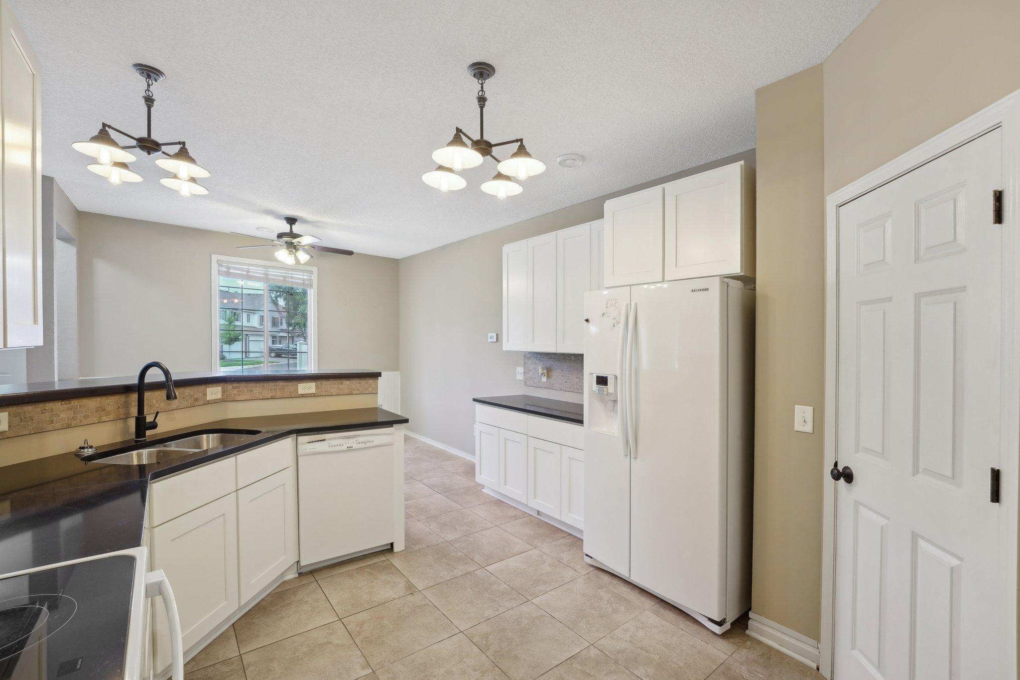 Kitchen with white cabinets, dark counters, tiled floor, and a breakfast bar beside a window.