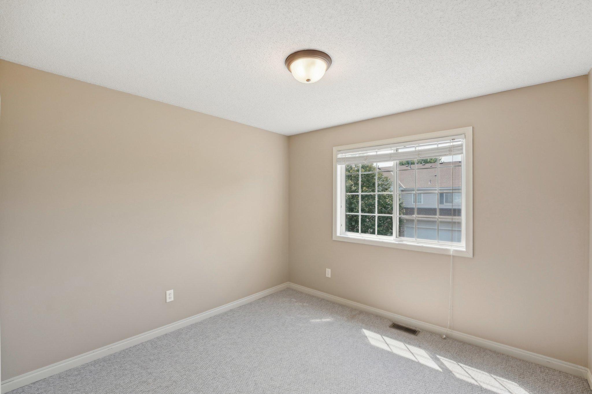 Empty carpeted room with beige walls and a sunny window.