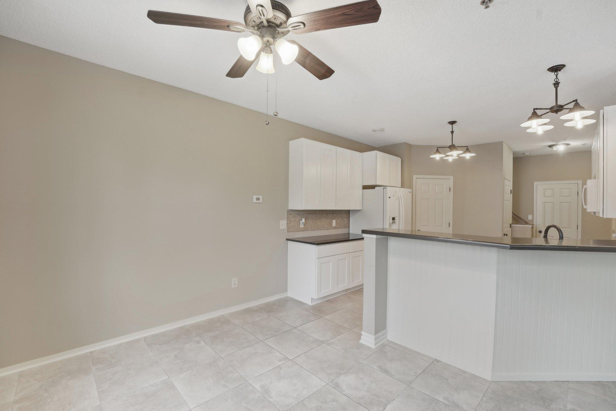 Kitchen with white cabinets, dark countertops, tiled floors, and a large peninsula breakfast bar.