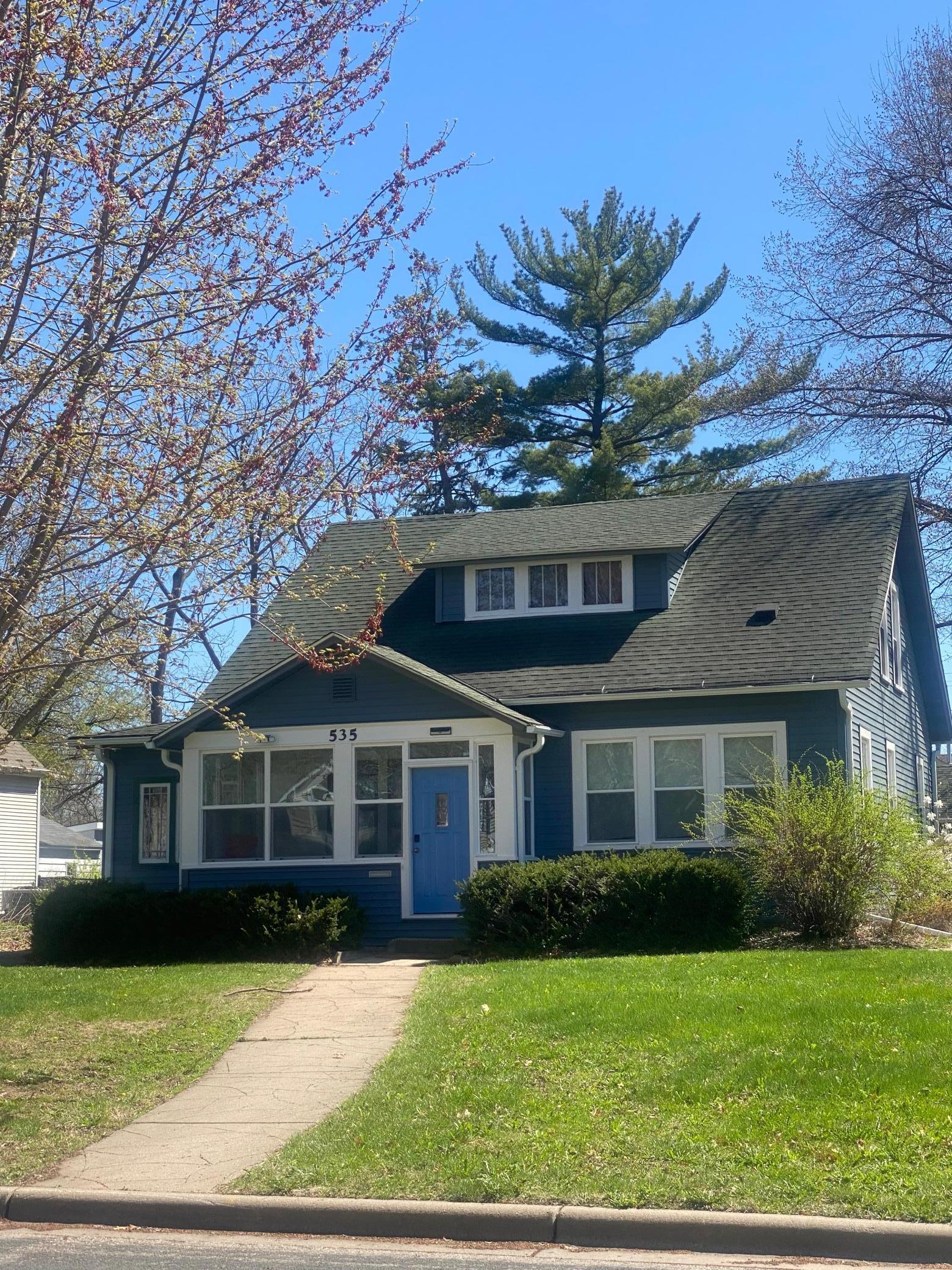 Blue two-story house with white-trimmed windows, a blue front door, and a steep roof with dormer.