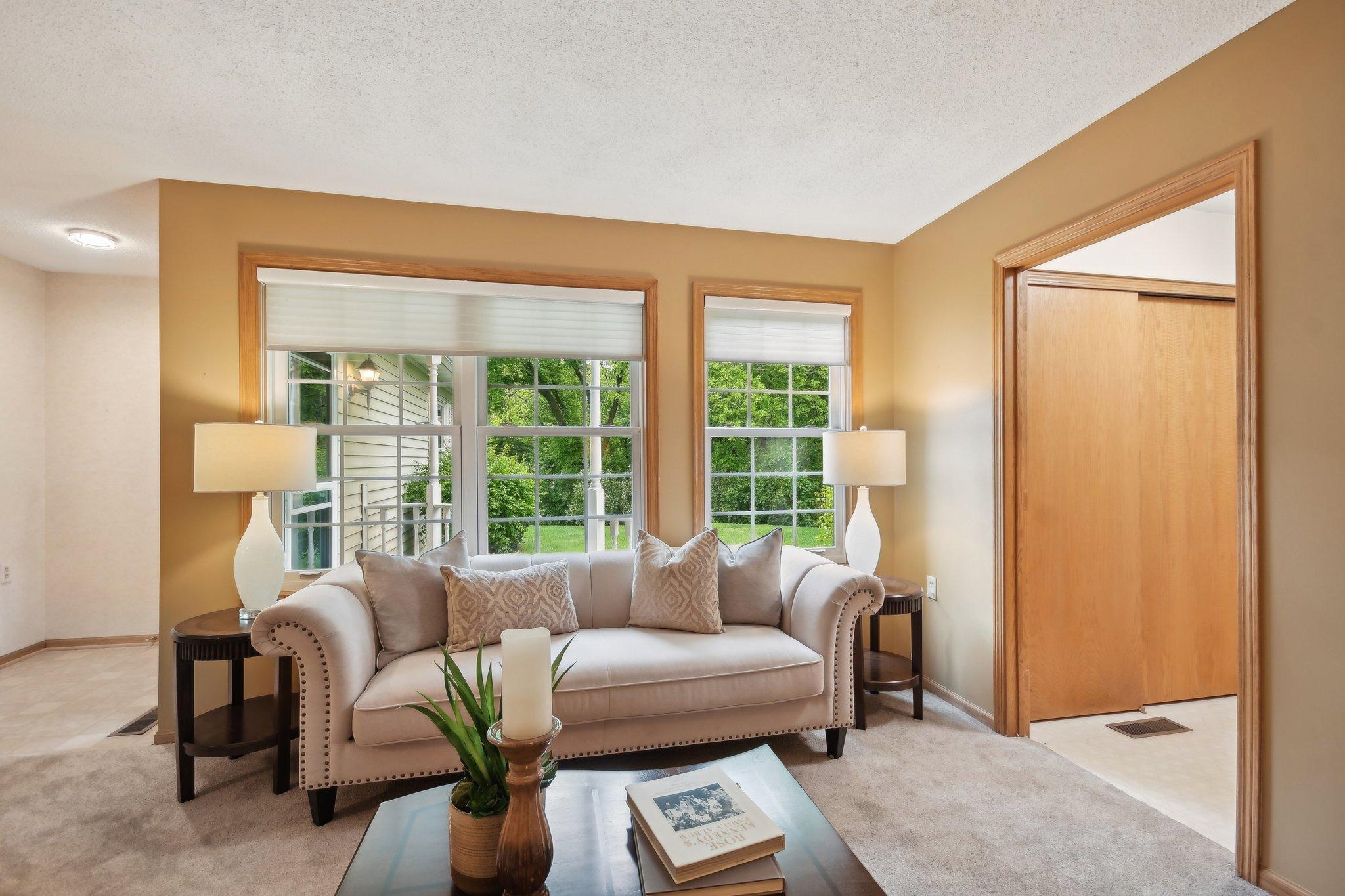 Living room with a light sofa, wood-trimmed windows, and greenery outside.