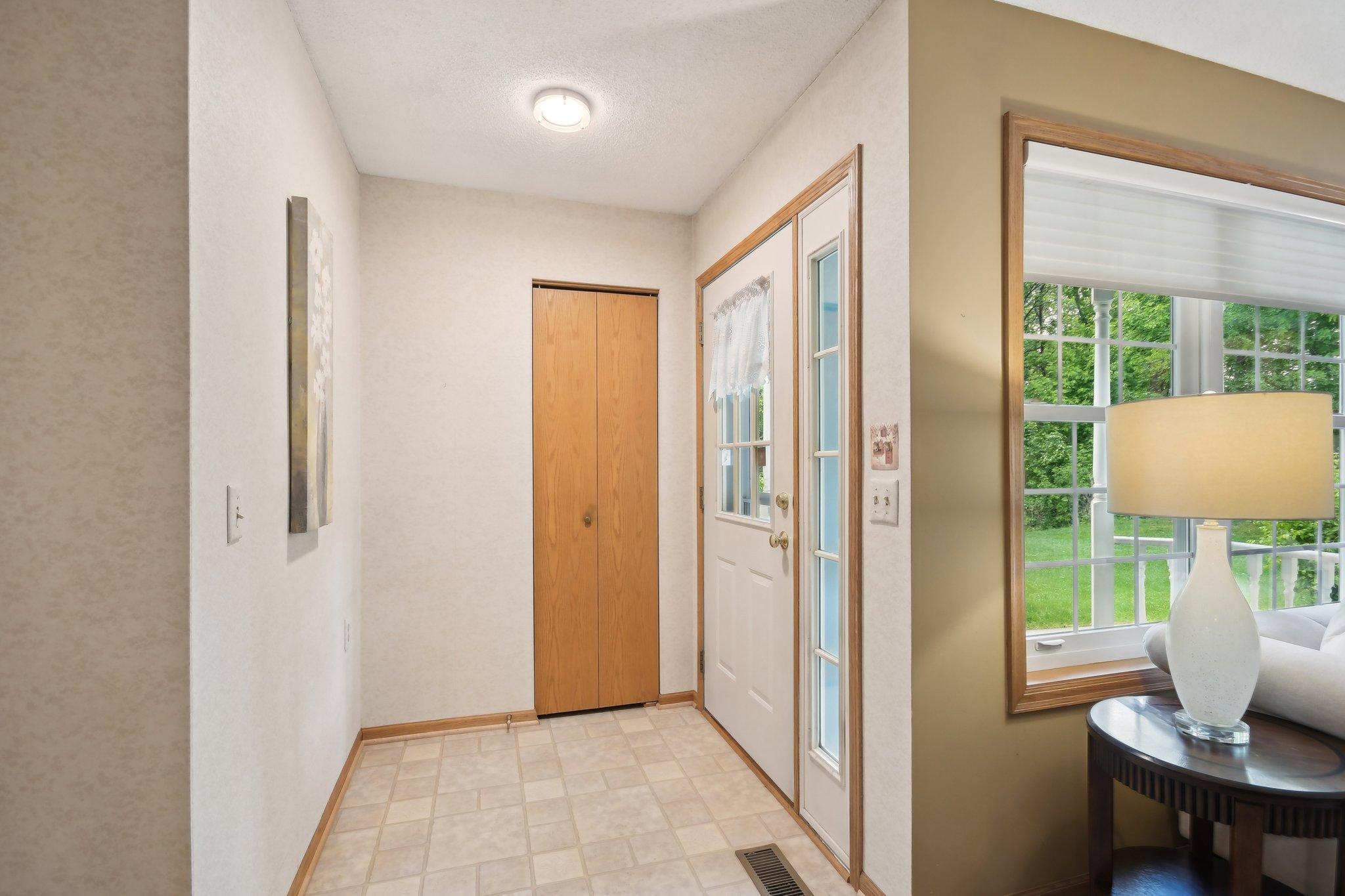 Entryway with tiled floor, wooden closet doors, and a white front door with glass sidelights.