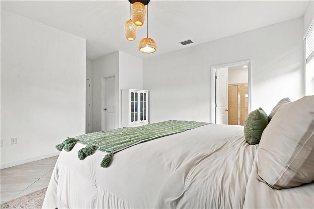 Staged bedroom with white bedding, a green throw, and three pendant lights.