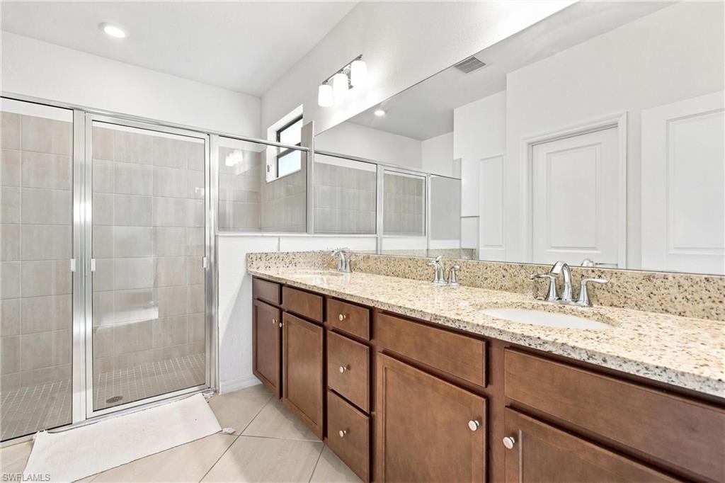 Bathroom with a double-sink granite vanity, dark wood cabinets, and a glass-enclosed shower.