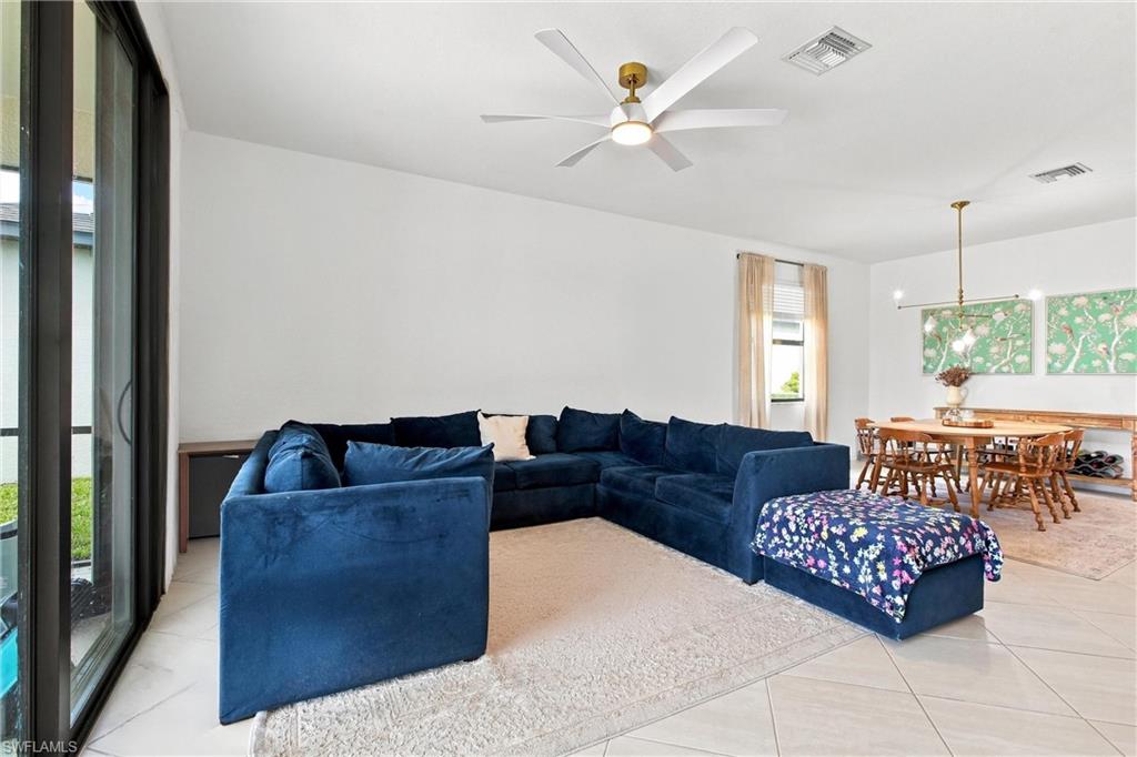 Open-plan living and dining area with a navy sectional, floral ottoman, and wooden dining set.
