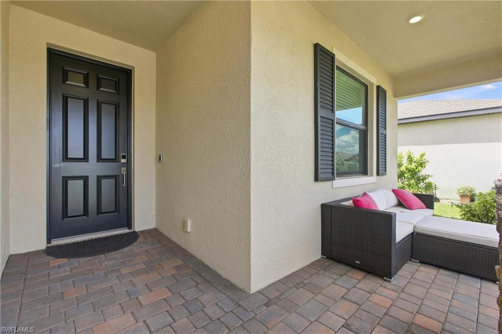 Covered front entry patio with a black door, paver flooring, and outdoor sectional seating.