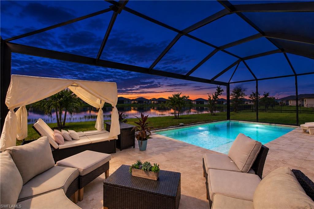 Screened pool lanai with cabana seating overlooking a lake at sunset.