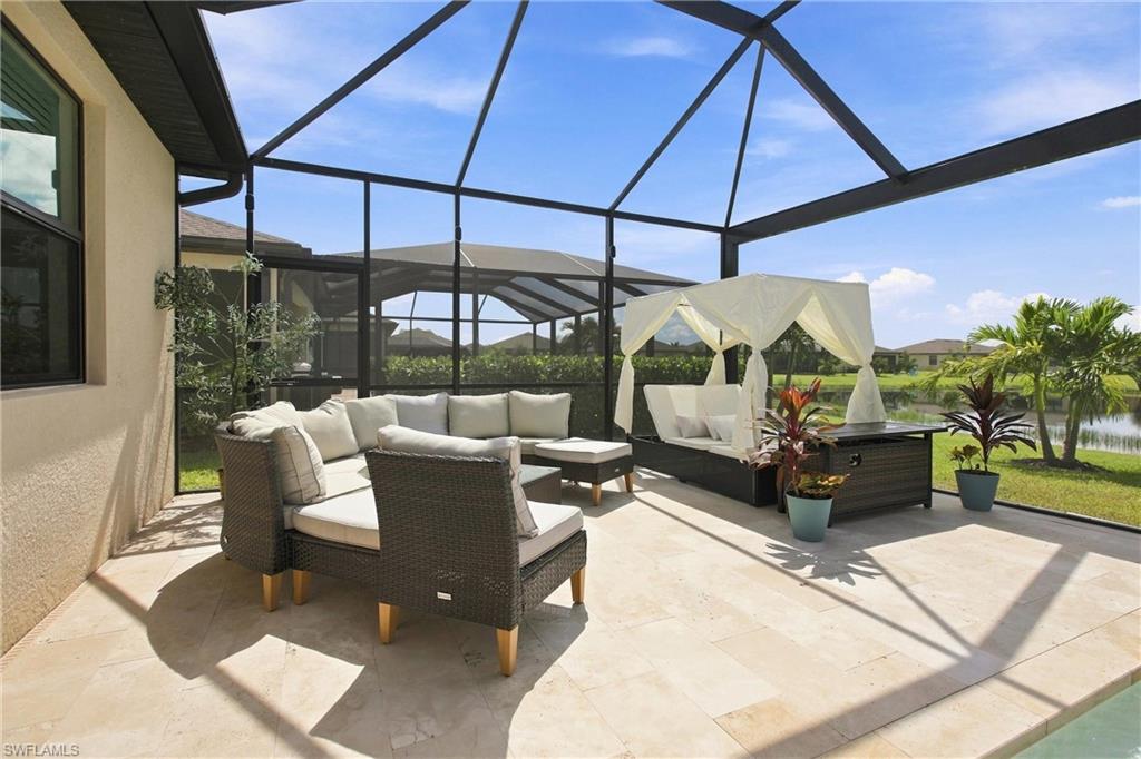 Screened lanai with wicker seating and a curtained daybed overlooking a small body of water.
