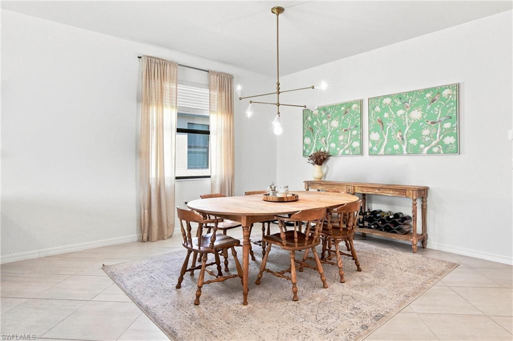 Dining room with a round wooden table, branching chandelier, and green floral artwork.