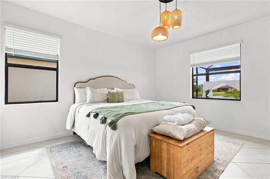 Bedroom with a white bed, green throw, wooden bench, and windows overlooking a covered patio.