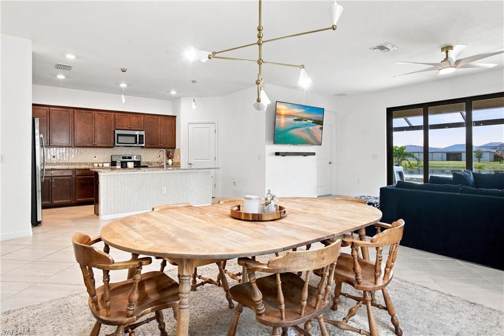 Open-plan dining room with a round wooden table, dark wood kitchen cabinets, and pond views through sliding doors.