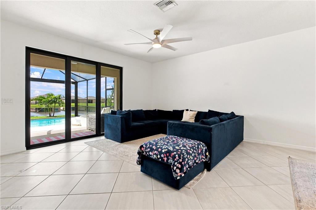 Living room with a dark blue sectional and floral ottoman overlooking a pool through sliding glass doors.