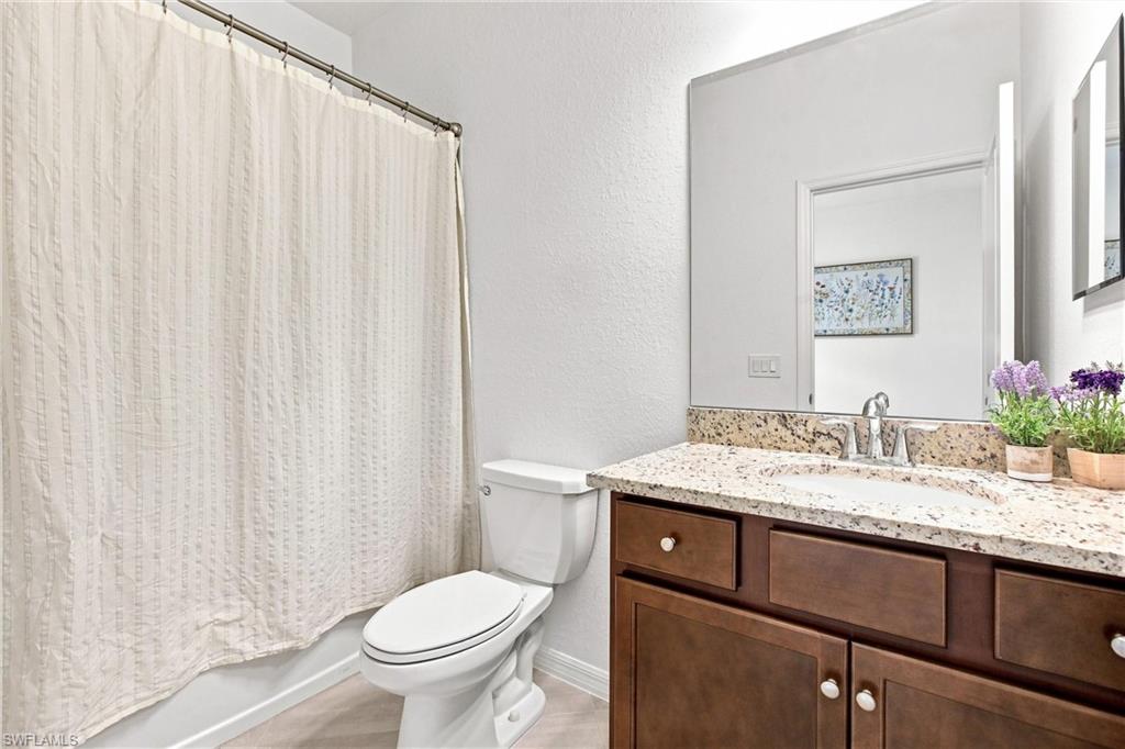 Bathroom with granite vanity, dark wood cabinets, and a curtained bathtub beside the toilet.