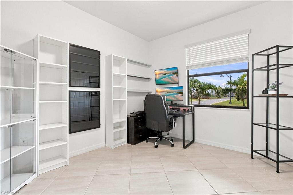Home office with built-in shelving, a desk, and a window overlooking palm trees.