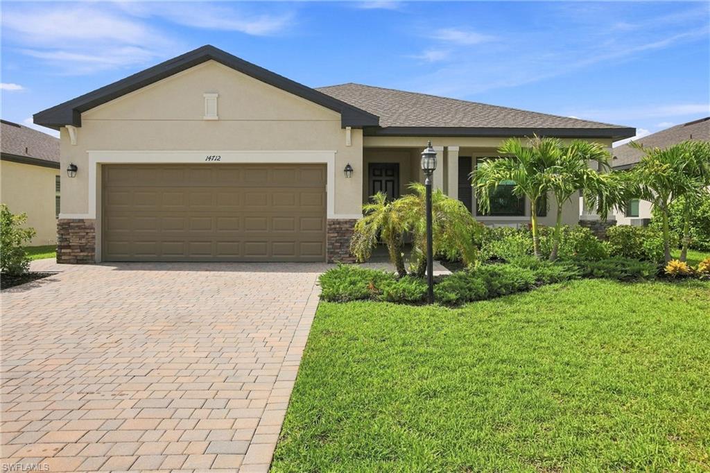 Single-story home with a two-car garage, paver driveway, and palm landscaping.