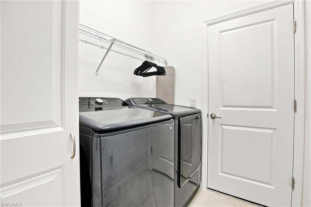 Laundry room with matching dark gray washer and dryer beneath a wire shelf.