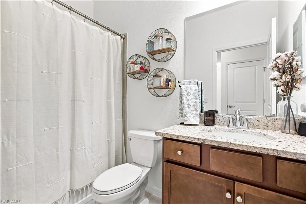 Bathroom with a brown vanity, speckled stone countertop, white toilet, and shower curtain.