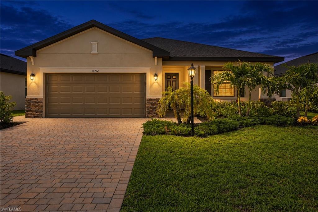 Single-story home at dusk with a wide paver driveway, two-car garage, and landscaped front lawn.