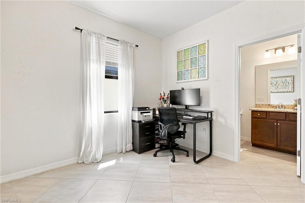 Furnished home office with a black desk and computer beside a curtained window.