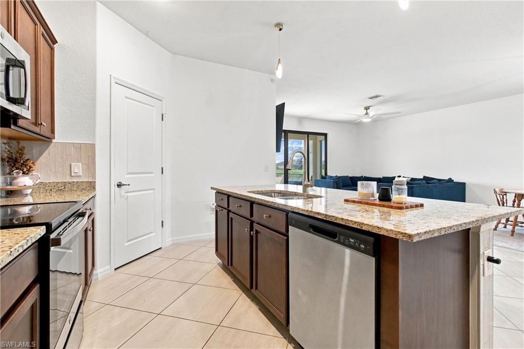 Kitchen with a large granite island, stainless steel dishwasher, and open view to a living room with a blue sofa.
