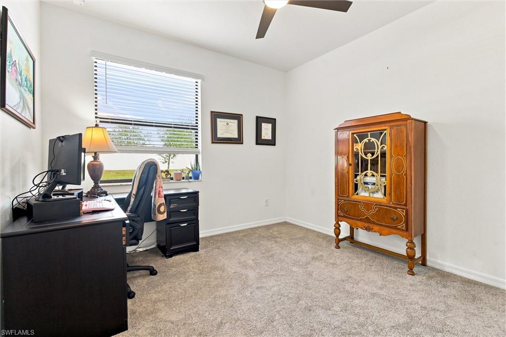 Home office with a dark computer desk, beige carpet, and ornate wooden display cabinet.