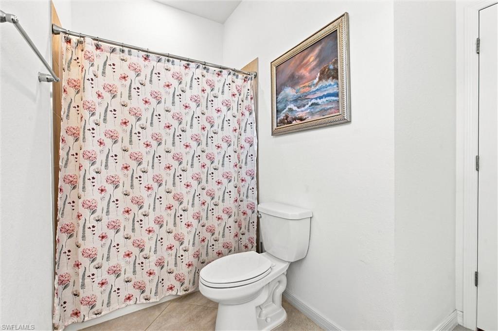 Bathroom with a white toilet, floral shower curtain, and framed seascape.