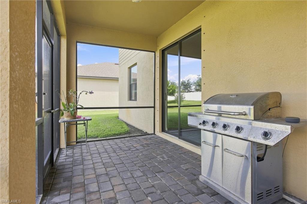 Covered paver patio with a stainless steel grill and sliding glass doors overlooking a lawn.