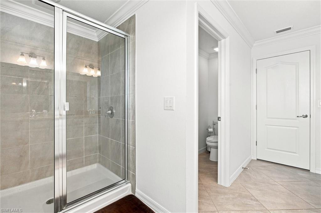 Bathroom with a glass-enclosed tiled shower and toilet visible through the doorway.