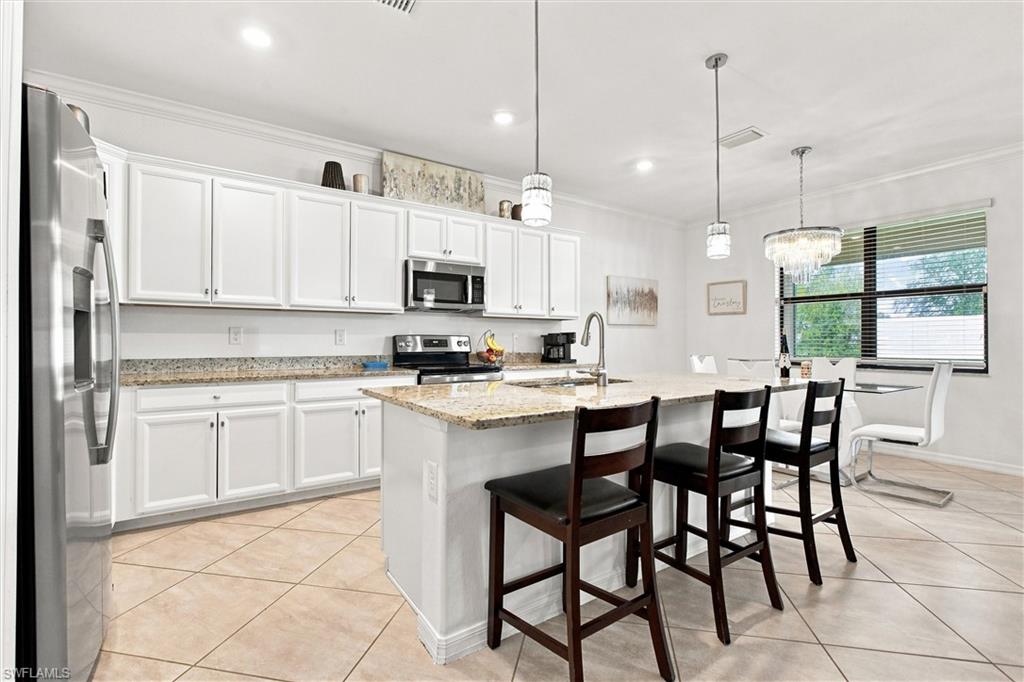 Kitchen with white cabinets, stainless appliances, and a granite island with bar stools.