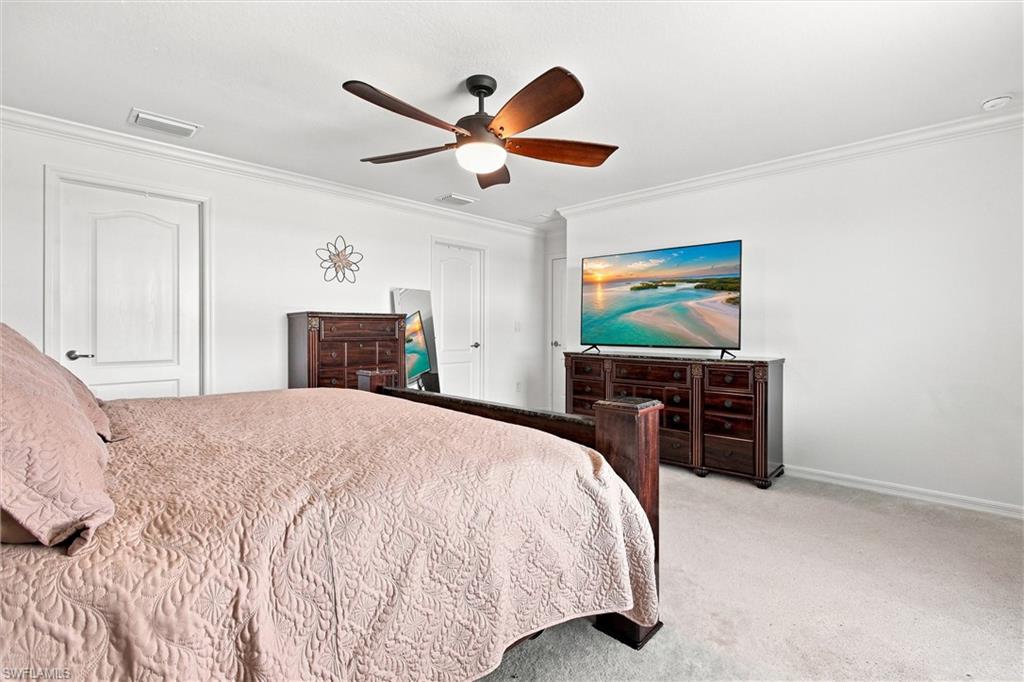 Bedroom with a pale quilted bed, dark wood furniture, and a ceiling fan.