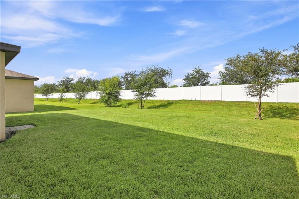 Backyard lawn with a white privacy fence, young trees, and the house at the left.