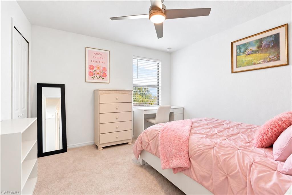 Bedroom with pink bedding, a cream dresser, and a desk beneath the window.