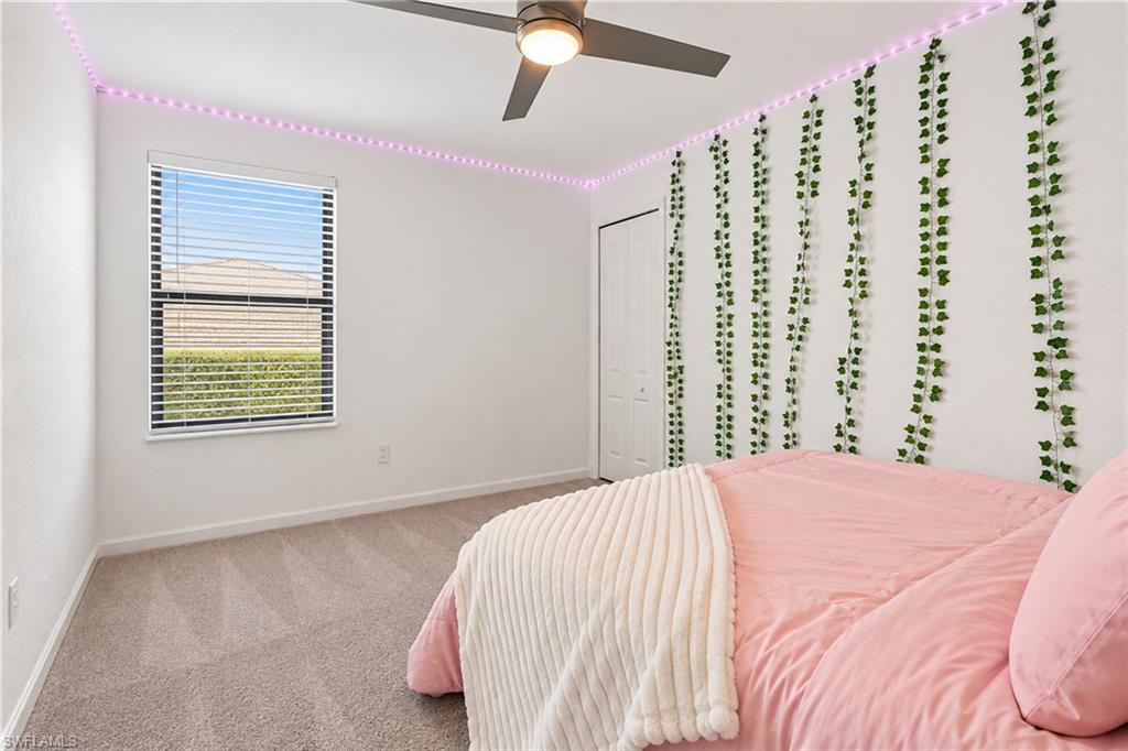 Bedroom with pink bedding, trailing green wall vines, purple ceiling lights, and a ceiling fan.