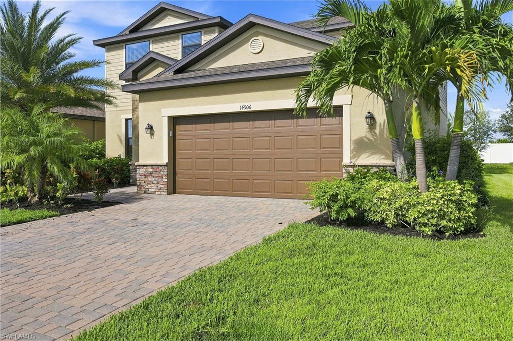 Two-story beige home with a brown double garage, paver driveway, and palm landscaping.