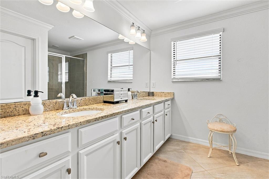 Bathroom with a white vanity, speckled granite countertop, large mirror, and shower reflected behind it.