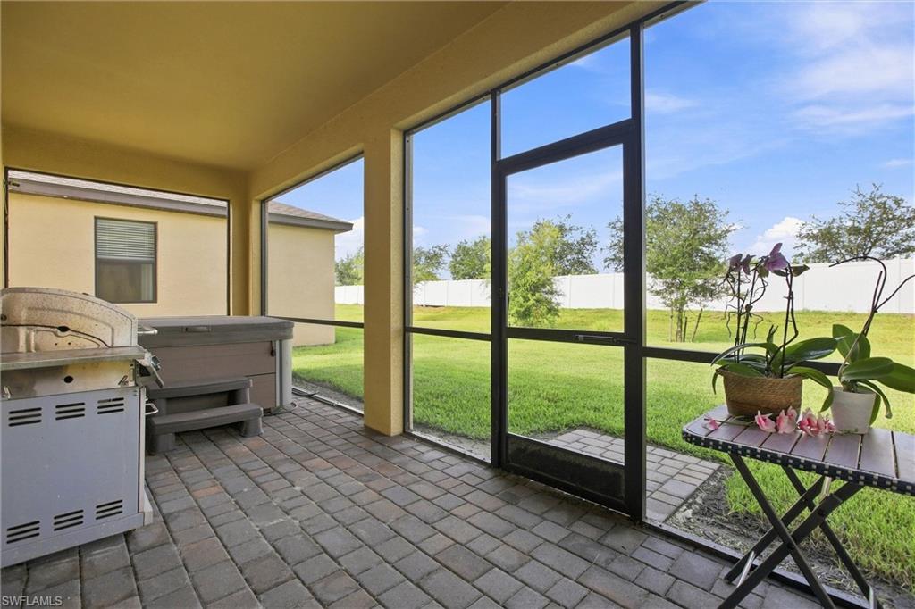 Screened patio with a grill and hot tub overlooking a fenced grassy backyard.