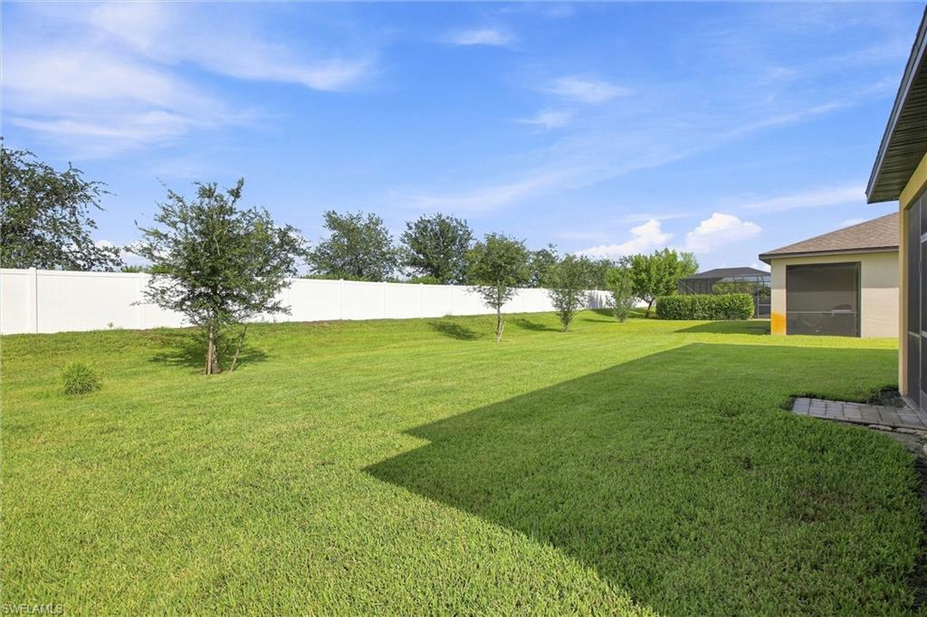 Spacious grassy backyard with young trees, a white privacy fence, and part of the house.