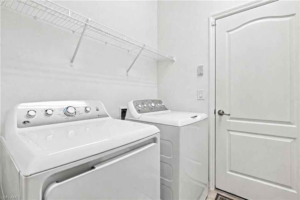 Laundry room with a top-loading washer and dryer beneath wire shelving.